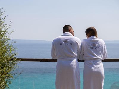 Dwie osoby w białych szlafrokach stoją na balkonie z widokiem na morze.