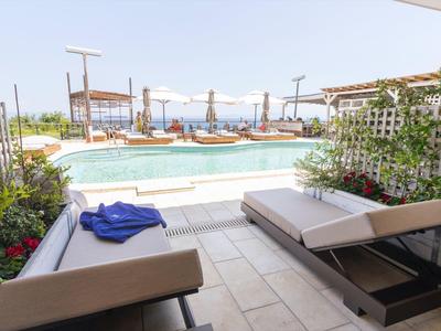 Strefa wypoczynkowa z leżakami z widokiem na basen i morze w tle.