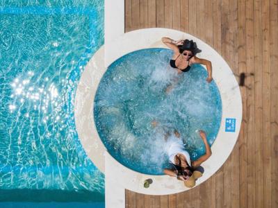 Dwie kobiety relaksują się w okrągłym jacuzzi obok prostokątnego basenu na drewnianym tarasie.