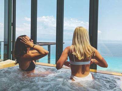 Dwie kobiety relaksują się w jacuzzi z widokiem na morze za dużymi szklanymi oknami.