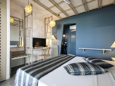 Modernes Hotelzimmer mit blauem Akzentwand, Doppelbett und TV mit Schreibtisch.