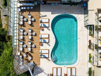 Vogelperspektive eines geschwungenen Pools neben Sonnenliegen und Tischen auf einer Hotelterrasse.