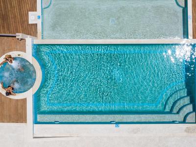 Vogelperspektive auf einen rechteckigen Pool mit blauer Wasseroberfläche und Holzterrasse.