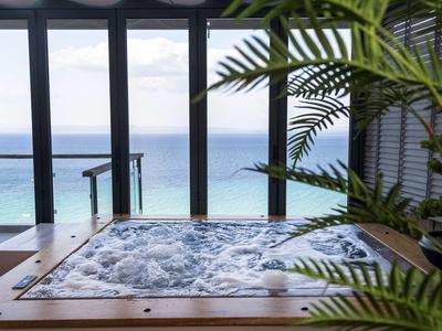 Ein Whirlpool mit Ausblick auf das Meer durch große Fenster in einem Hotelzimmer.