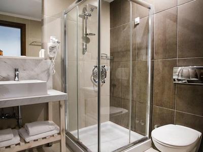 Jasna łazienka z szklaną kabiną prysznicową, wiszącą toaletą i dużą umywalką z ręcznikami pod spodem.