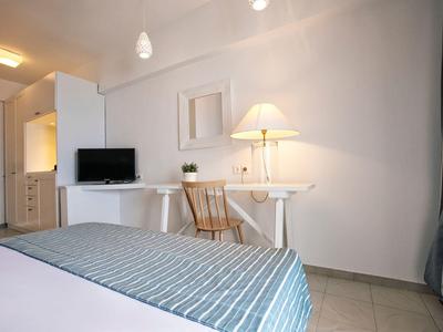 Nowoczesny pokój hotelowy z białym biurkiem, krzesłem, telewizorem i łóżkiem z niebieską narzutą.