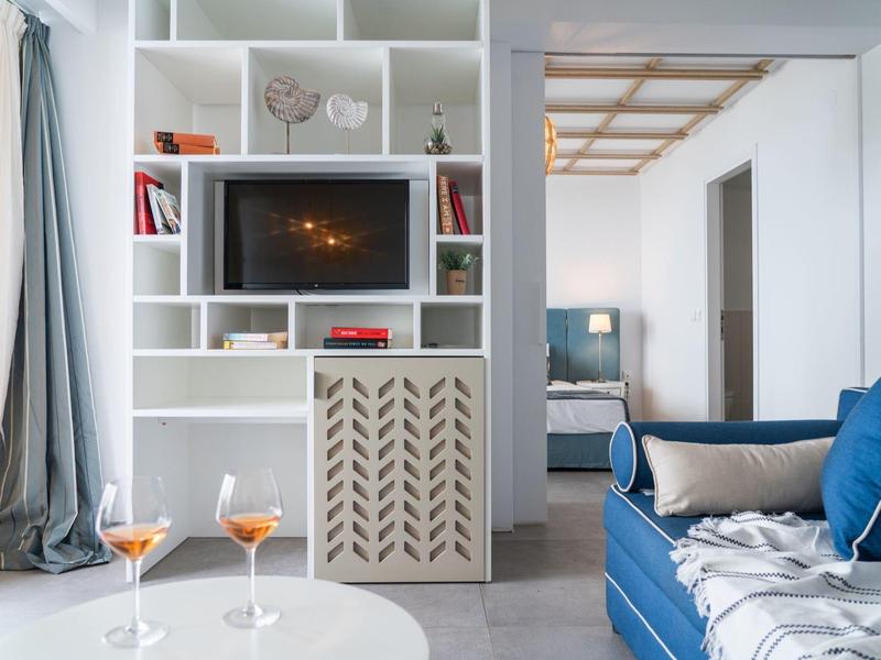 Nowoczesny salon z białą półką, telewizorem, niebieską sofą i dwoma kieliszkami wina na stole.