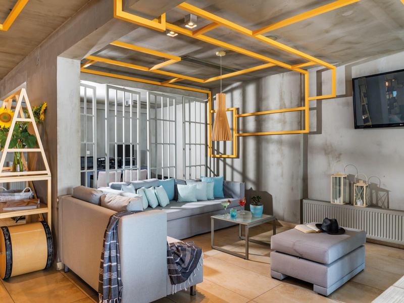 Nowoczesny salon z szarą sofą, pufą i jaskrawożółtymi rurami sufitowymi.