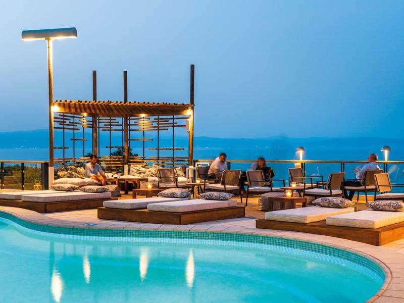 Nowoczesny basen z leżakami i pergolą przy morzu o zachodzie słońca.