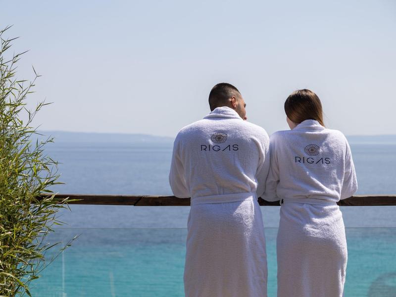 Dwie osoby w białych szlafrokach stoją na balkonie z widokiem na morze.