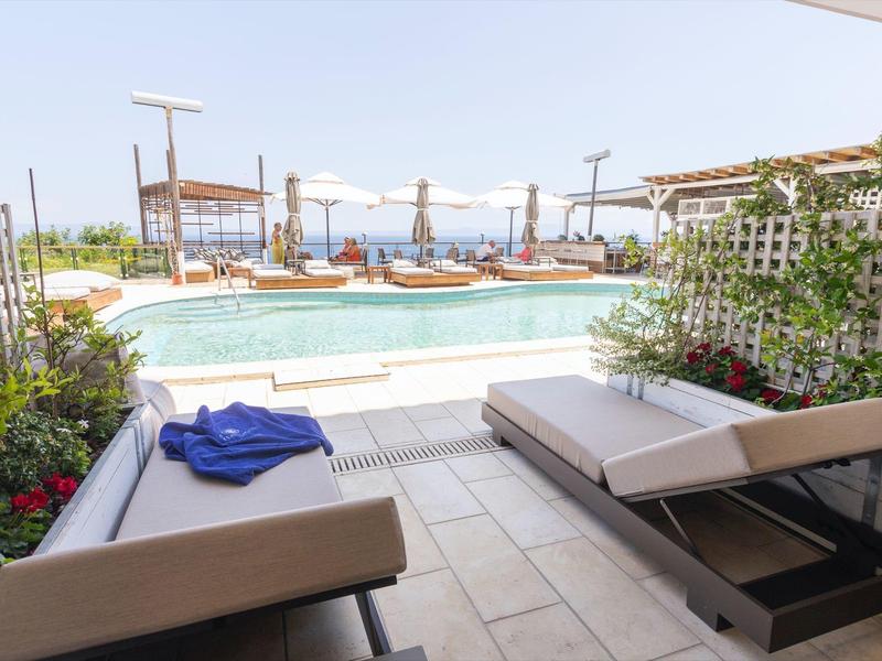 Strefa wypoczynkowa z leżakami z widokiem na basen i morze w tle.