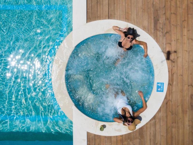 Dwie kobiety relaksują się w okrągłym jacuzzi obok prostokątnego basenu na drewnianym tarasie.