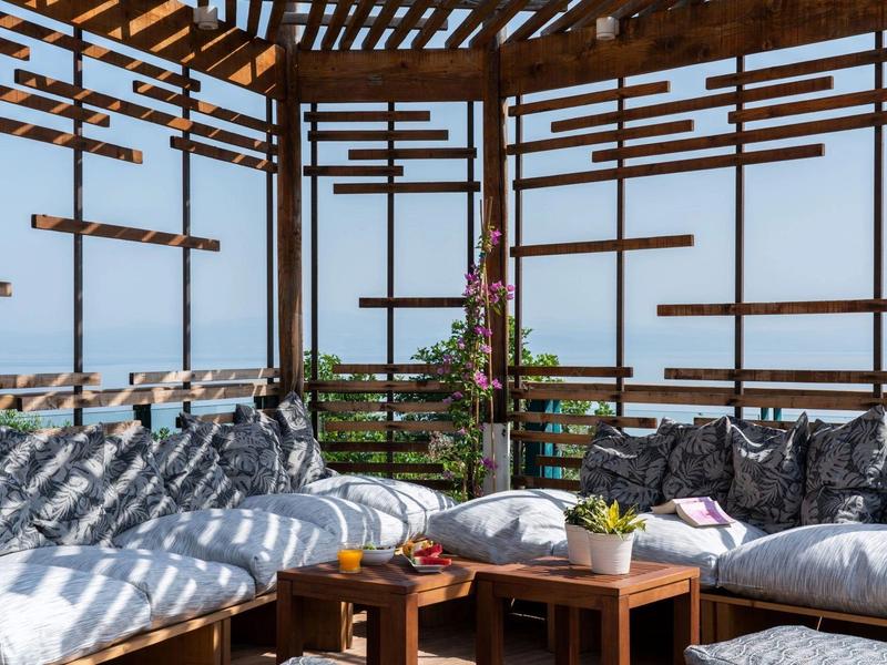 Otwarta strefa wypoczynkowa z meblami drewnianymi, poduszkami i widokiem na morze pod drewnianym dachem