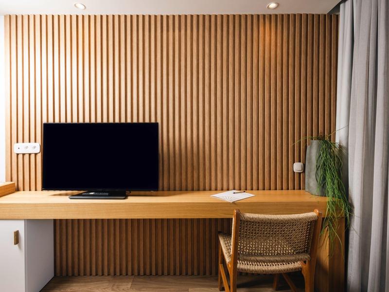Nowoczesne miejsce pracy w hotelu z drewnianymi panelami, biurkiem, krzesłem, telewizorem i zasłoną.