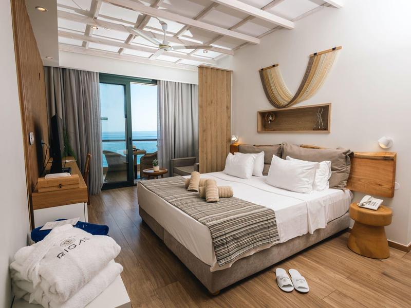 Nowoczesny pokój hotelowy z dużym łóżkiem, widokiem na morze i drewnianymi detalami w ciepłym świetle.