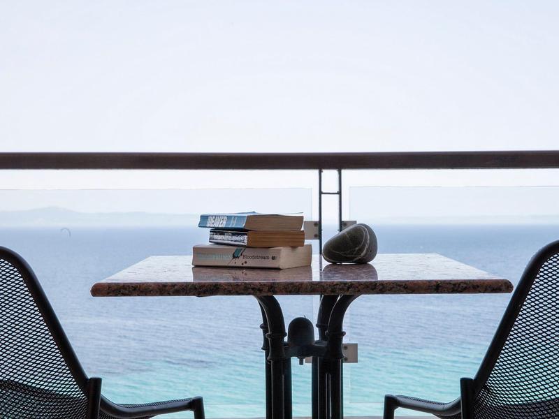 Stolik dla dwóch osób z książkami i muszlą na balkonie z widokiem na morze.