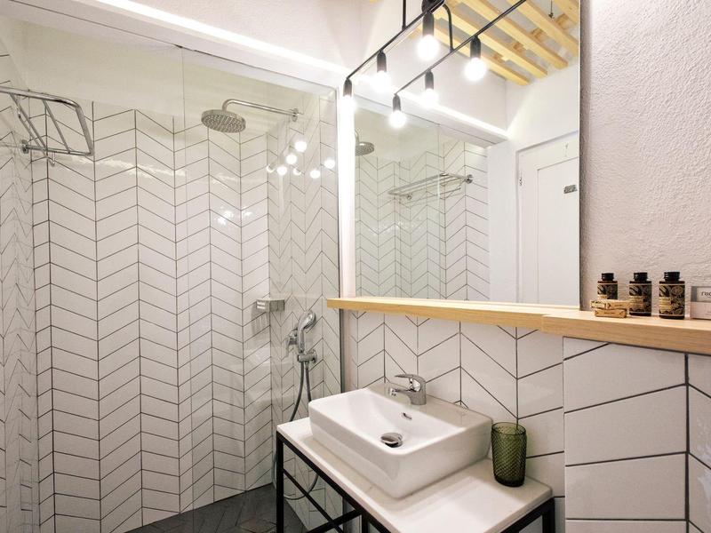 Jasna łazienka z prysznicem bez drzwi, umywalką na czarnej ramie i dużym podświetlanym lustrem.