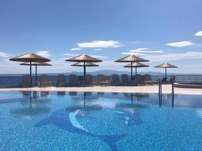 Piscina a sfioro con ombrelloni e vista sul mare sotto un cielo azzurro.