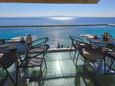 Blick von einer Terrasse mit Tischen und Stühlen auf das Meer und einen hellen Horizont.