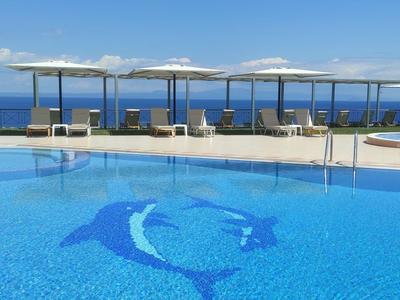 Großer Pool mit Delfinmosaik, Liegen und Blick auf das Meer bei klarem Himmel.