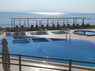 Ein Hotelpool mit Sonnenliegen und Blick auf das Meer bei klarem Himmel.