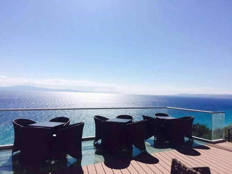 Buitenzitplaatsen op balkon met uitzicht op kalme blauwe zee onder heldere lucht.