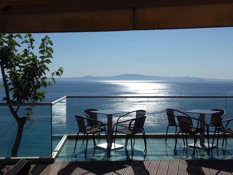 Lege tafels en stoelen buiten met uitzicht op een kalme zee en verre bergen.