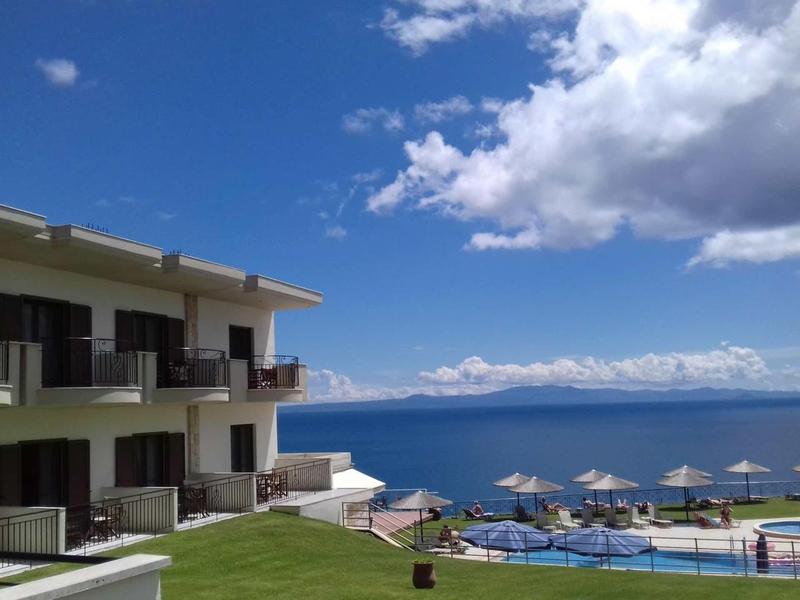Hotel aan zee met balkons over zwembad en oceaan onder half bewolkte lucht.