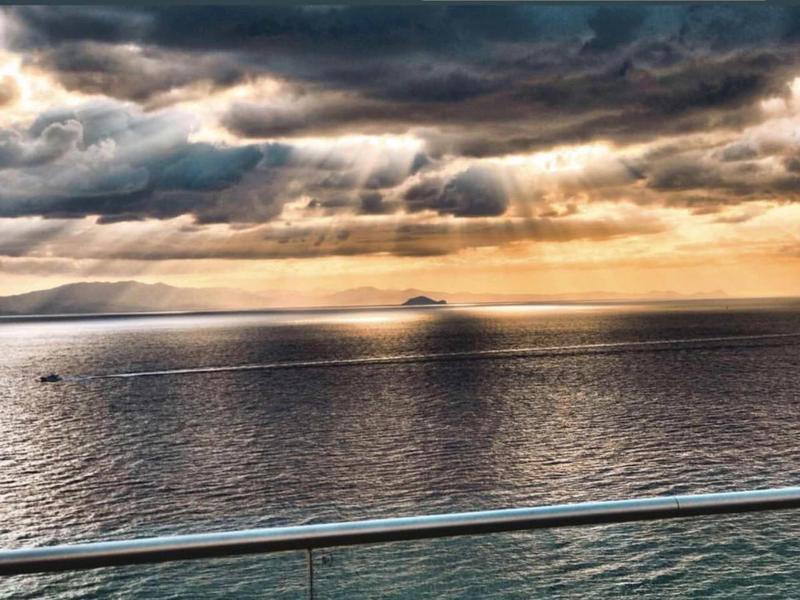Zonnestralen breken door wolken boven kalme zee met verre eilanden en metalen reling op de voorgrond