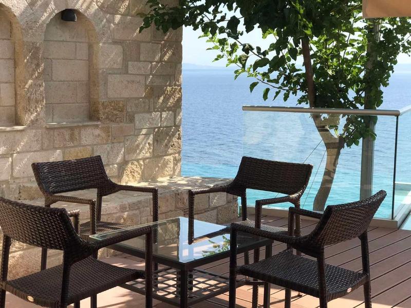 Terras buiten met wicker stoelen en glazen tafel met uitzicht op oceaan vanaf houten dek