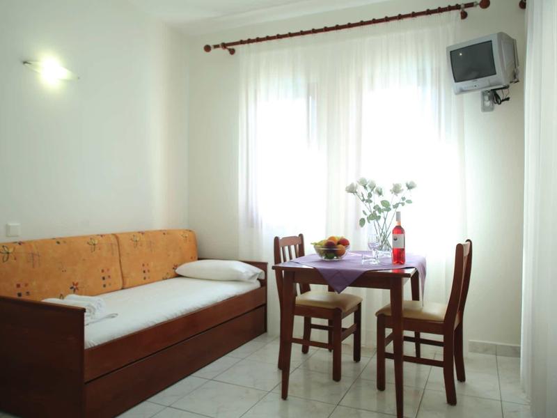 Kleiner Raum mit Holzsofa, Tisch mit Stühlen, hellem Vorhang und einer Wandlampe.