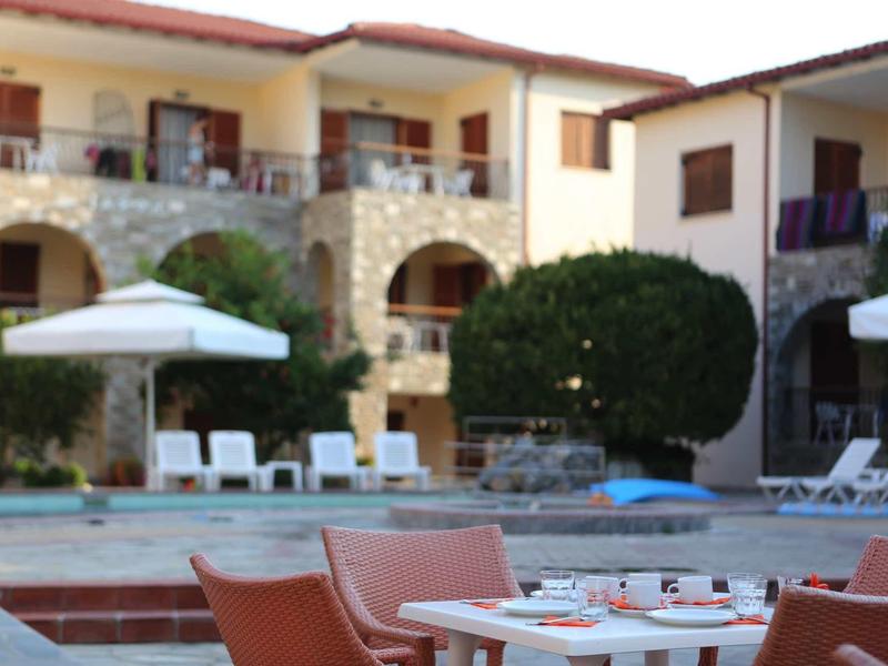 Hotel mit Pool, Liegestühlen, Sonnenschirmen und Tischen mit Stühlen im Außenbereich.