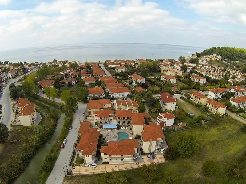 Luftaufnahme einer Siedlung mit roten Dächern, Straßen, Bäumen und Hügeln im Hintergrund.
