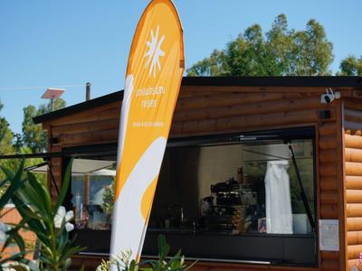 Holzgebäude mit offener Servicefläche und orangefarbenem Werbebanner vor grünem Hintergrund.