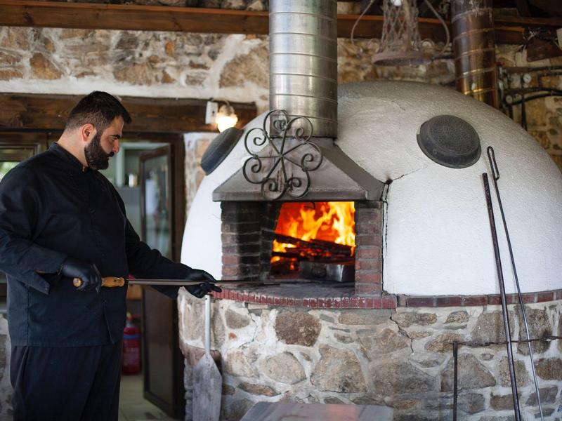 Een man gebruikt een schop om vers hout in een stenen en bakstenen oven te leggen.