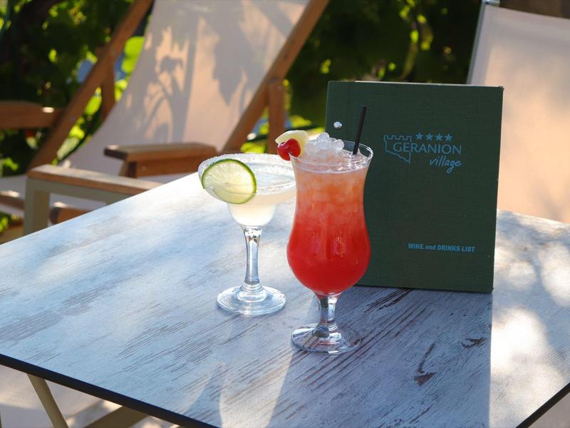 Tafel met twee cocktails en een drankkaart, ligstoelen in zonlicht erachter.