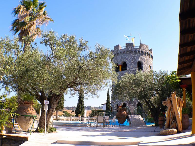 Toren in mediterrane omgeving met olijfbomen en palmbomen onder een heldere hemel