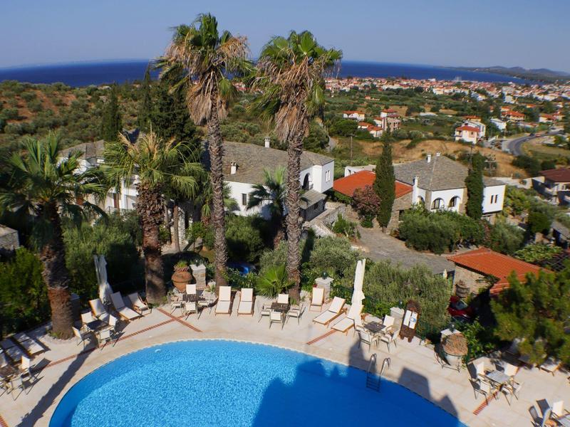 Uitzicht op een zwembad met parasols en palmbomen in een vakantiepark nabij zee en stad.