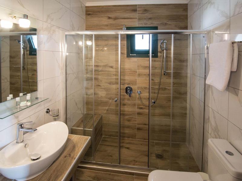 Compacte badkamer met glazen douchecabine, witte wastafel en houten accenten.