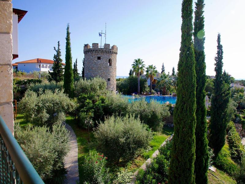 Uitzicht op een tuin met cipressen en een ronde toren op de achtergrond bij helder weer.