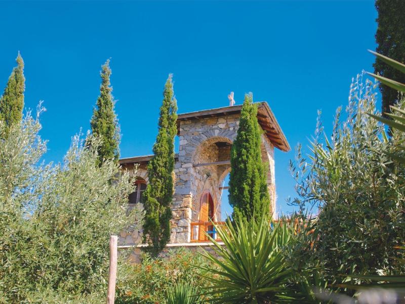 Historisch stenen gebouw omgeven door bomen onder een heldere blauwe hemel.
