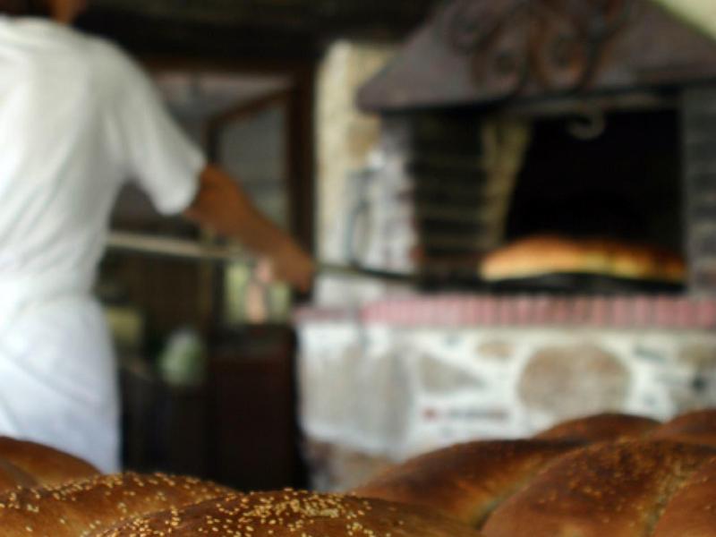 Verschillende versgebakken broden op de voorgrond met een bakker bij de oven op de achtergrond