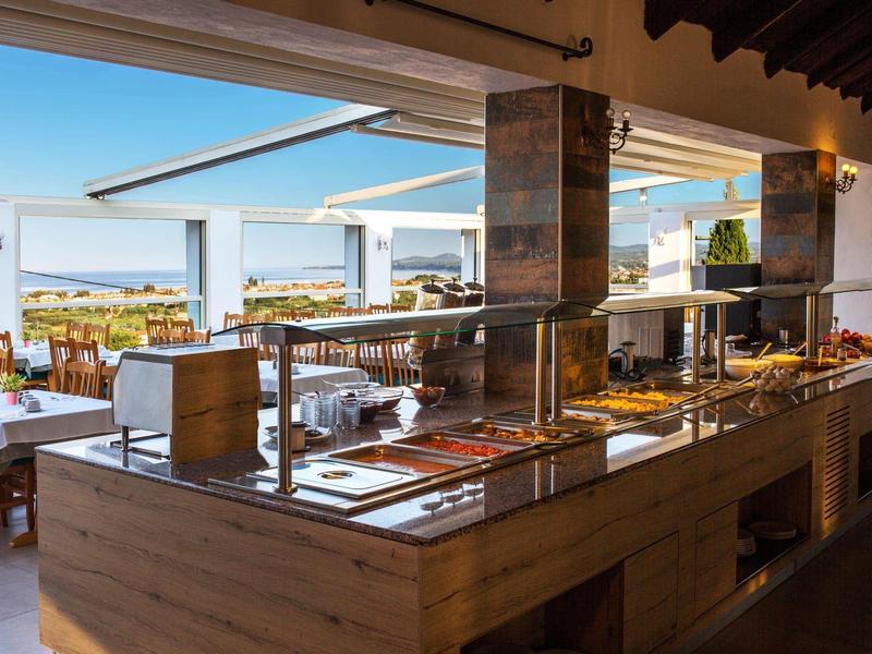 Buffetgedeelte met warme gerechten, houten tafels en zeezicht op een hotelterras.