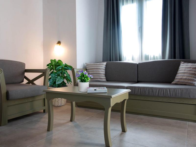 Gezellige hotel- of woonruimte met fauteuils, bank, tafel en planten bij een raam met gordijnen.