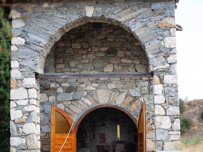 Kleine stenen kapel met open houten deuren en een kruis op het dak.