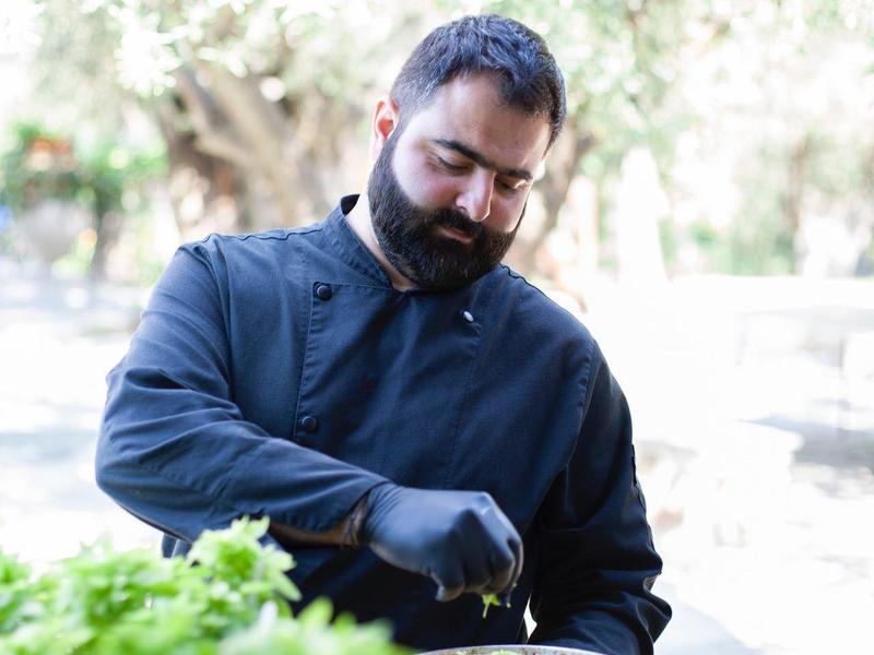 Man bereidt buiten een pizza met zwarte handschoenen.