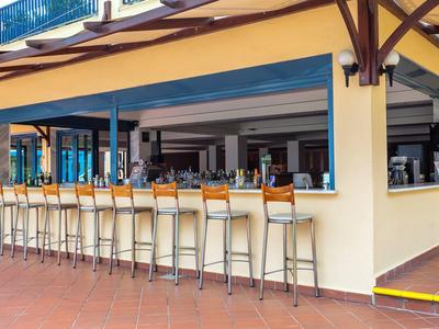 Bar al aire libre con taburetes altos y paredes amarillas en una zona de hotel.