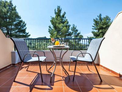 Balcón acogedor con dos sillas, vasos y jugo frente a un bosque verde de pinos.
