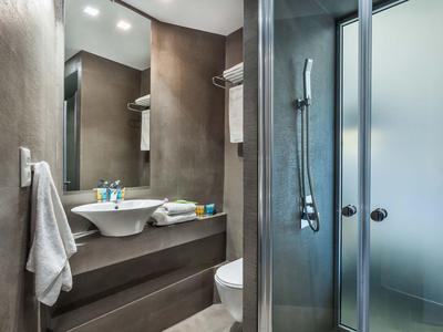 Baño moderno con ducha de vidrio, lavabo, toallas y decoración limpia y elegante.