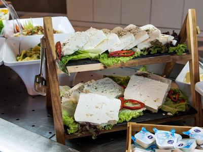 Estantería de dos niveles con varios sándwiches y guarniciones en una zona de buffet.